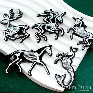 May include: A collection of black and white skeleton animal charms, including a deer, horses, and a mermaid. The charms are displayed on a white, textured surface against a dark green background. The Happy Supplies logo is visible.