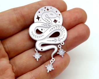 May include: A silver-colored pendant featuring a stylized snake design with a crescent moon and star accents. The snake is coiled, with three dangling star charms. The pendant is held in a hand against a white background.