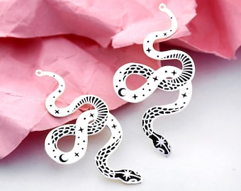 May include: Two silver snake charms with a black and white design of a snake with stars and a crescent moon. The charms have a loop at the top for attaching to jewelry.