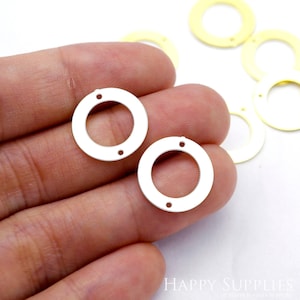 以下が含まれることがあります： 2つの穴がそれぞれ開いた銀色の金属製の円形。円形の直径は約2.5cmです。