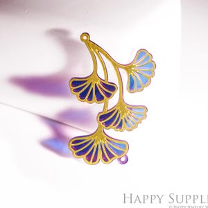 Könnte beinhalten: Ein goldfarbener Metallanhänger mit einem Ginkgo-Blatt-Design. Die Blätter sind mit blauem und violettem Emaille verziert. Der Anhänger hat oben eine kleine Schlaufe zum Befestigen an Schmuck oder anderen Bastelarbeiten.