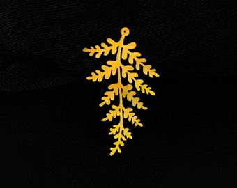 May include: Gold-colored metal fern charm with a hole at the top for hanging. The charm is in the shape of a fern frond with delicate details.