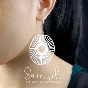 Peut inclure: Boucles d'oreilles en argent avec un motif g&eacute;om&eacute;trique en forme de soleil. Les boucles d'oreilles sont suspendues &agrave; l'oreille d'une personne.