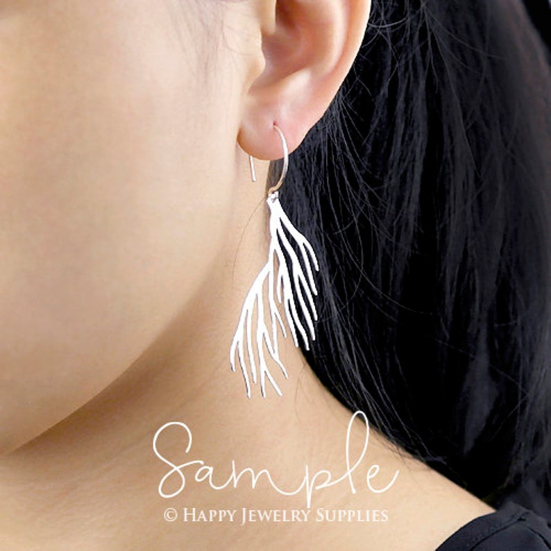 Peut inclure: Boucles d'oreilles pendantes en argent avec un design d&eacute;licat en forme de branche. Les boucles d'oreilles sont pr&eacute;sent&eacute;es sur l'oreille d'un mannequin.