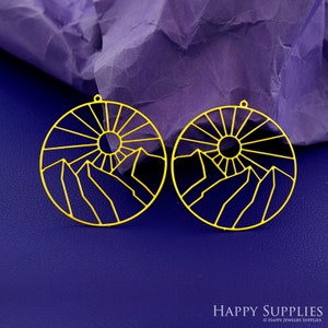 May include: A pair of gold-colored metal earrings with a sun and mountain design. The earrings are circular and have a delicate wire frame.