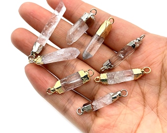 May include: A collection of eight clear quartz crystal pendants with gold and silver accents. The pendants are in the shape of a long, thin point. They are perfect for jewelry making.