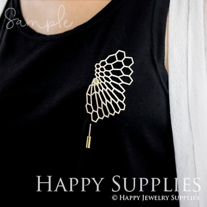 May include: A gold-toned geometric brooch in the shape of a fan, with a pin on the back. The brooch is on a black shirt.