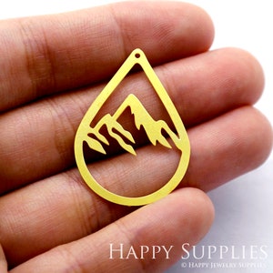 Op de afbeelding: Gouden metalen hanger in de vorm van een traan met een berg silhouet erin.