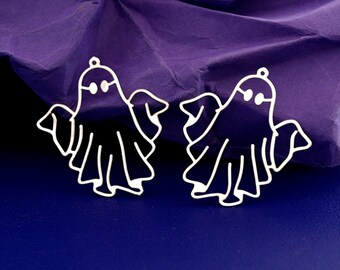 Pode incluir: Dois pingentes prateados em forma de fantasma com um pequeno laço na parte superior para pendurar. Os fantasmas têm características simples e arredondadas e um design recortado. O fundo é uma superfície azul escuro com papel roxo amassado.