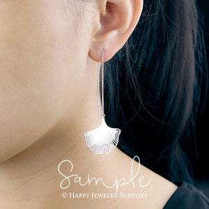 May include: Silver dangle earrings with a delicate ginkgo leaf design. The earrings are long and feature a thin chain with a small leaf charm at the bottom.