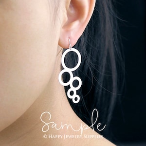 May include: Silver dangle earrings with a design of multiple interlocking circles. The earrings are shown on a model's ear.
