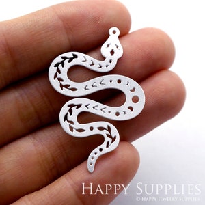 Op de afbeelding: Zilveren metalen slangenbedel met een uitgesneden ontwerp met bladeren en geometrische vormen. De bedel heeft een gat aan de bovenkant om aan sieraden te bevestigen.