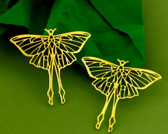 Pode incluir: Dois pingentes de borboleta de metal dourado com um design delicado e intrincado. Os pingentes são recortados na forma de uma borboleta com asas detalhadas e um corpo.