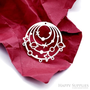 May include: A silver metal charm in the shape of a circle with a design of planets and stars. The charm is on a red crumpled paper background.