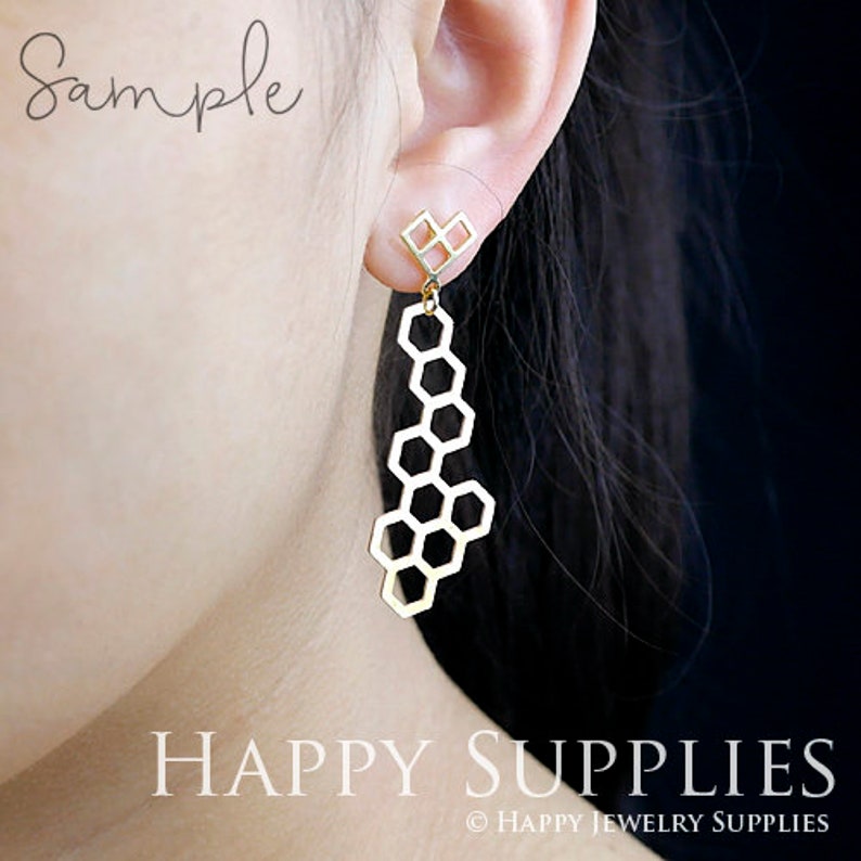 Peut inclure: Boucles d'oreilles g&eacute;om&eacute;triques en forme de nid d'abeille dor&eacute;es avec un petit charme en forme de diamant en haut. Les boucles d'oreilles sont pendantes et ont un design d&eacute;licat et moderne.