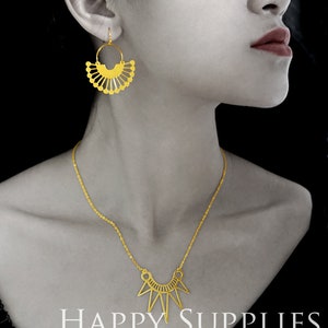 May include: A gold necklace with a geometric pendant and a matching pair of gold earrings with a fan-shaped design. The jewelry is displayed on a model with a black background. The text "HAPPY SUPPLIES" is displayed at the bottom of the image.