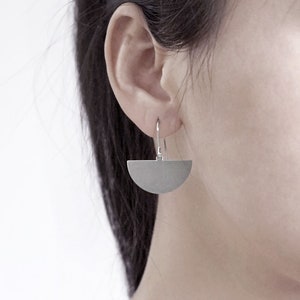 May include: A pair of silver half-circle earrings with a simple design. The earrings are hanging from a person's ear.