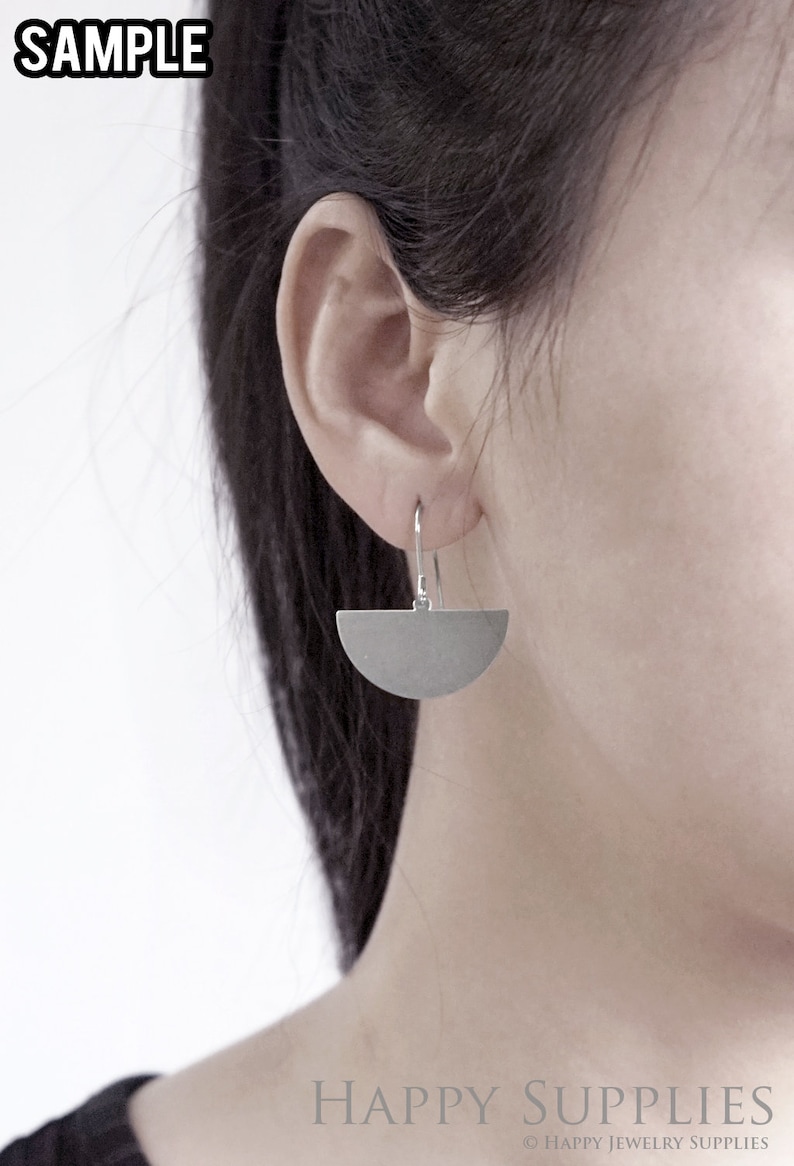 May include: A pair of silver half-circle earrings with a simple design. The earrings are hanging from a person's ear.