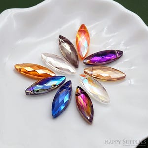 Puede incluir: Surtido de 10 cuentas de cristal iridiscente en forma de lágrima en varios colores, incluyendo transparente, morado, azul, naranja y dorado. Las cuentas están dispuestas en círculo sobre una superficie blanca.