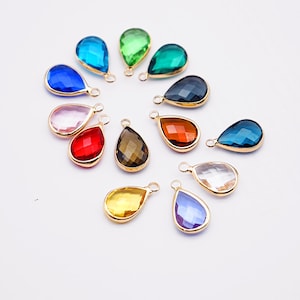 Puede incluir: Una colección de colgantes de piedras preciosas en forma de lágrima en varios colores, incluyendo azul, verde, rojo y amarillo. Cada colgante tiene un marco de metal dorado y un pequeño lazo para sujetarlo a una cadena u otra pieza de joyería.