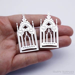 Puede incluir: Dos colgantes plateados con forma de ventana gótica. Cada colgante presenta una parte superior arqueada con intrincados diseños recortados, incluyendo un cuadrifolio central y barras verticales. Los colgantes tienen un pequeño lazo en la parte superior.