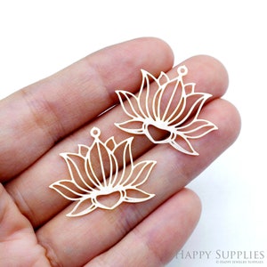 Könnte beinhalten: Zwei silberne Metall-Lotusblüten-Anhänger mit einem Loch oben zum Aufhängen. Die Anhänger sind filigran und detailliert gearbeitet.