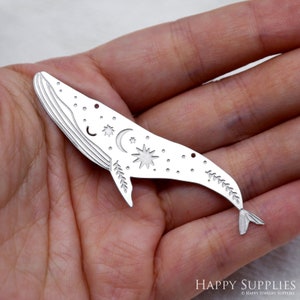 以下が含まれることがあります： 星、月、葉の細かなデザインが施されたシルバーのクジラチャーム。クジラの上部に吊り下げ用の穴があります。