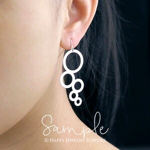 May include: Silver dangle earrings featuring a design of multiple interlocking circles. The earrings are shown on a model's ear.