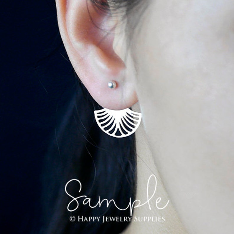 May include: A pair of silver earrings with a delicate fan-shaped design. The earrings are shown on a model's ear.