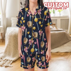 May include: Navy blue short pajama set with a baseball theme. The set features a button-down shirt and shorts, both adorned with baseballs, bats, gloves, bows, and hearts. The text "CUSTOM Short Pajama Set" is visible at the top.