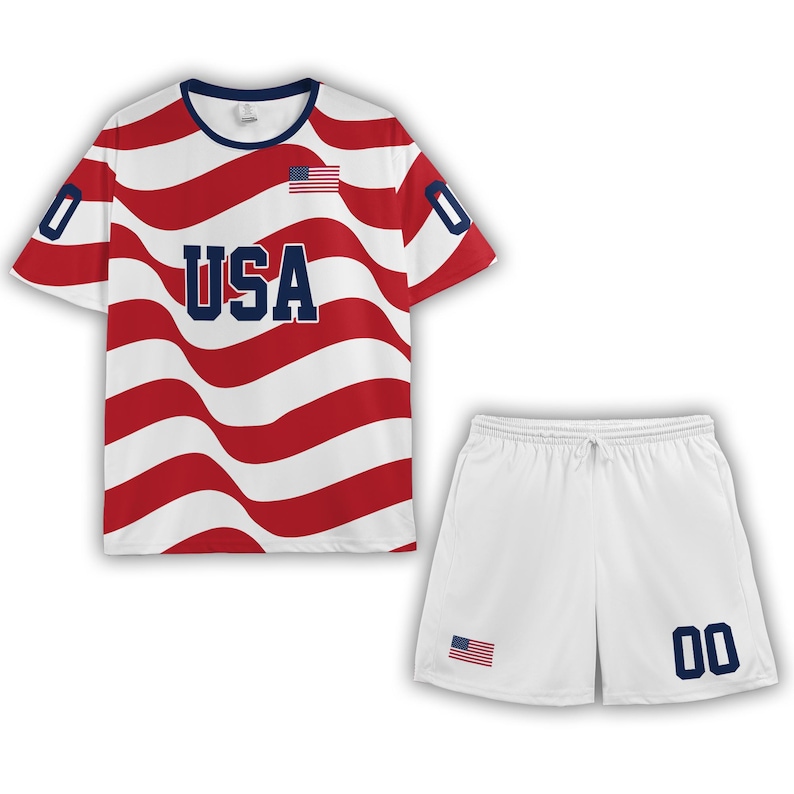 Puede incluir: Un conjunto de camiseta de manga corta y pantal&oacute;n corto con un patr&oacute;n de rayas onduladas rojas y blancas. La camiseta muestra el texto USA en azul, una peque&ntilde;a bandera estadounidense y el n&uacute;mero 0 en cada manga. El pantal&oacute;n blanco tiene una bandera y 00.