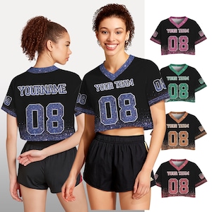 Puede incluir: Top corto negro con cuello en V y n&uacute;meros y ribetes azules brillantes. El texto "YOUR TEAM" y "08" son visibles en la parte delantera. La parte trasera de la camiseta tiene el texto "YOURNAME" y "08".