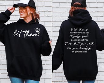 Op de afbeelding: Zwart hoodie met een witte vlinder afbeelding en de tekst "let them" op de voorkant. De achterkant van de hoodie heeft de tekst "let them Misunderstand you Judge you Gossip about you Never doubt your worth or your beauty Be you & shine."