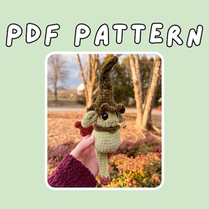 May include: A crocheted doll with a pointed hat, a green body, and a brown collar. The doll has small ears and a long, slender body. The text "PDF PATTERN" is displayed at the top of the image.