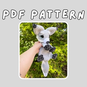 May include: A crocheted gray fox with black accents on its ears and paws. The fox has a white muzzle and a fluffy tail. The image includes the text "PDF PATTERN" in a bubble font.
