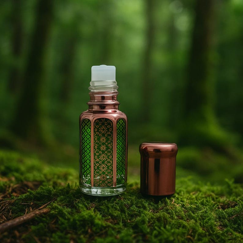 Mosswood Oud perfume oil bottle standing upright with the cap placed beside it, featuring a decorative metallic green and copper design, set against a clean white background with subtle forest elements for a natural and earthy presentation.
