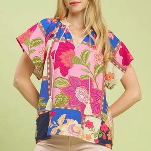 May include: A colorful floral print top with a V-neckline and short sleeves. The top features a mix of pink, blue, and cream-colored floral patterns. The text "BLUE MIX" is visible at the bottom right.