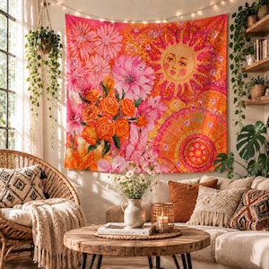 May include: A rectangular wall tapestry featuring a vibrant print of pink and orange flowers alongside a stylised sun with a human face. The design incorporates warm hues of yellow, orange, and pink, creating a bold, colourful visual display.