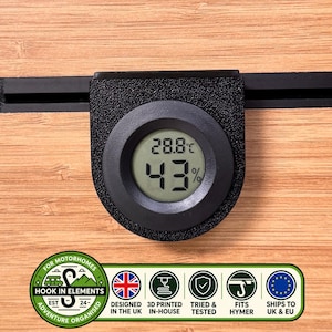 Pode incluir: Um termómetro e higrómetro digital preto circular que mostra 28,8 graus Celsius e 43 por cento de humidade. Abaixo, uma etiqueta retangular apresenta o texto Hook In Elements, Designed in the UK, 3D Printed In-House, Tried & Tested, Fits Hymer e Ships to UK & EU.