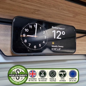 Può includere: Uno smartphone nero montato su una superficie con venature del legno che mostra un quadrante analogico, la località Rotherham, una temperatura di 12 gradi e il meteo Mostly Sunny con indicatori di temperatura massima e minima di 16 e 8 gradi.