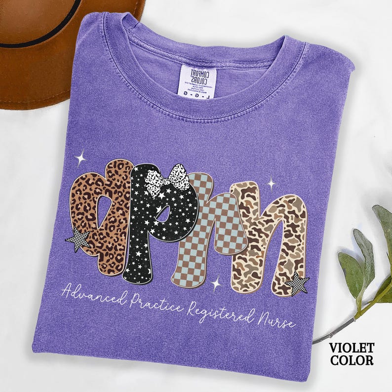 May include: A violet t-shirt featuring the letters "APRN" in a decorative style. The letters are patterned with leopard print, stars, and checkered designs. The text "Advanced Practice Registered Nurse" is printed below the letters in white.