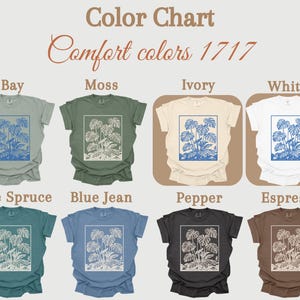 May include: A color chart displays eight t-shirts in various colors: Bay, Moss, Ivory, White, Blue Spruce, Blue Jean, Pepper, and Espresso. Each shirt features a blue and white botanical design within a rectangular frame. The text "Color Chart" and "Comfort colors 1717" are at the top.