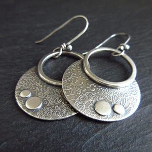 May include: A pair of silver earrings with a floral design and small round accents. The earrings are made of metal and have a hoop design.