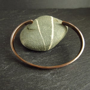 bronze oval shape cuff bangle leaning on pebble