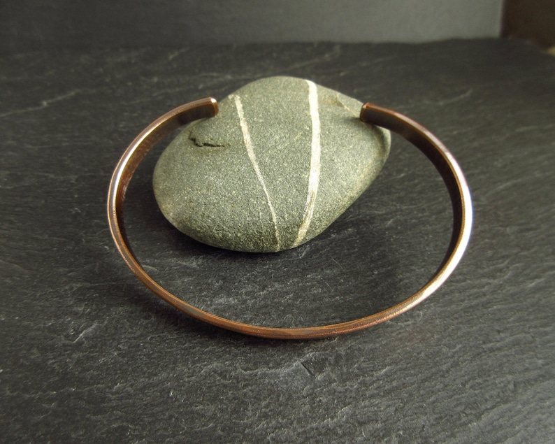 bronze oval shape cuff bangle leaning on pebble