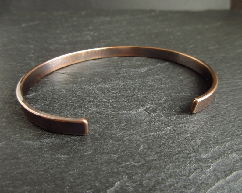 oval shape bronze cuff bangle showing the smooth inside texture sitting on a piece of slate