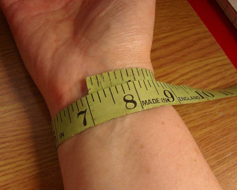 close up of inside of wrist with green tape measure wrapped around wrist to demonstrate how to measure for a cuff bangle.