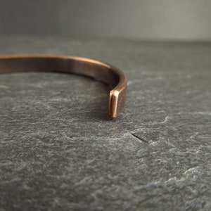 close up of end of bronze metal cuff bracelet on top of a piece of slate