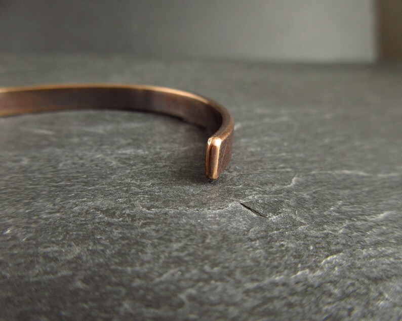 close up of end of bronze metal cuff bracelet on top of a piece of slate