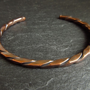 May include: A copper bracelet with a twisted design. The bracelet is made from a single piece of copper that has been twisted and shaped into a circle.